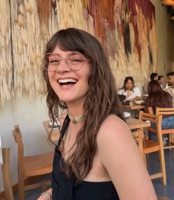 Anna, smiling, in front of a colourful restaurant tapestry
